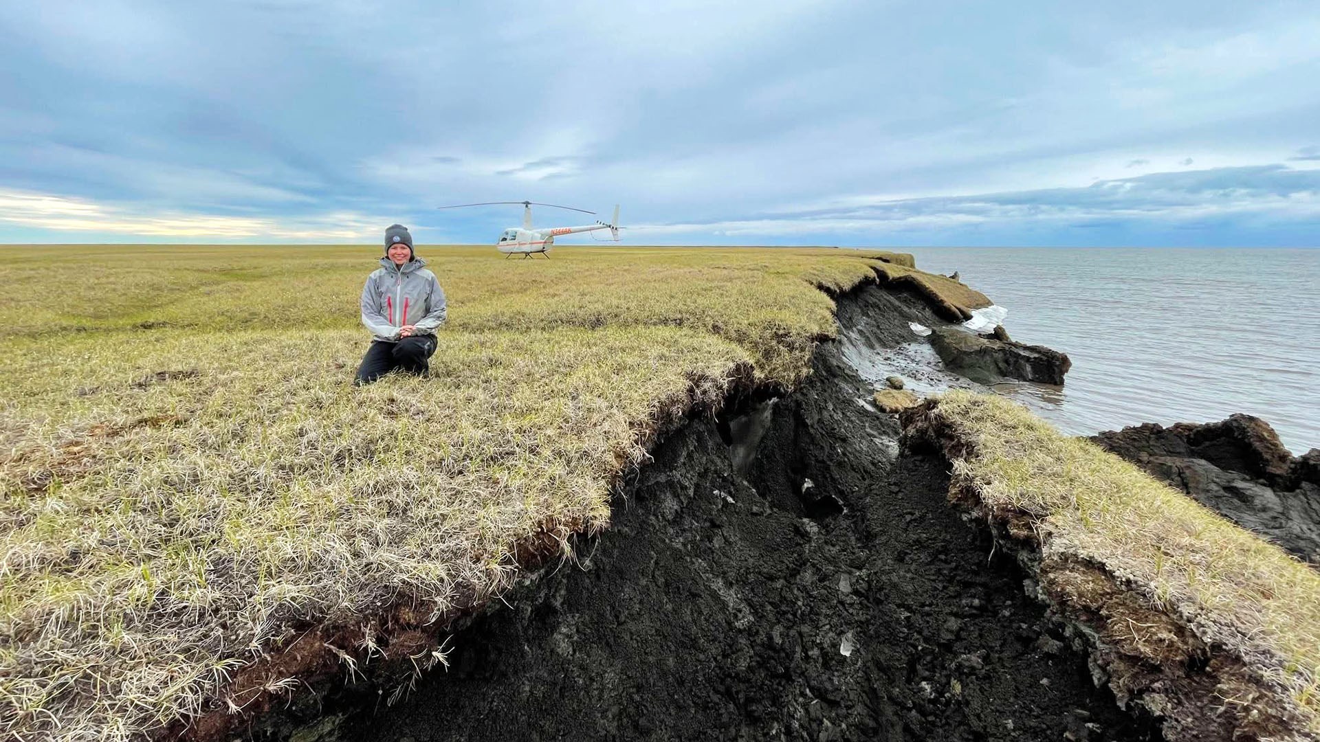 Melissa Ward Jones sits at the bluff edge at Drew Point, Alaska next to a collapse permafrost block in July 2021. UAF/INE photo by Benjamin Jones.