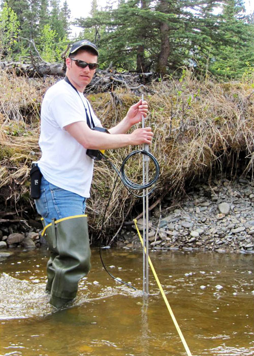 Researcher with hip waders standing creek measuring run offon glacier