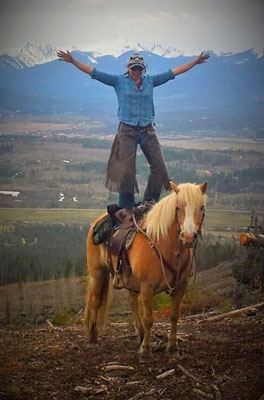Tiffany stan ding on top of horse with mountain backdrop